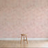 A single wooden stool sits on a light wooden floor against a pale pink wall decorated with Painted Cloud Stars Wallpaper, Rose, featuring subtle celestial patterns and white speckles in a softly lit, minimalistic scene.