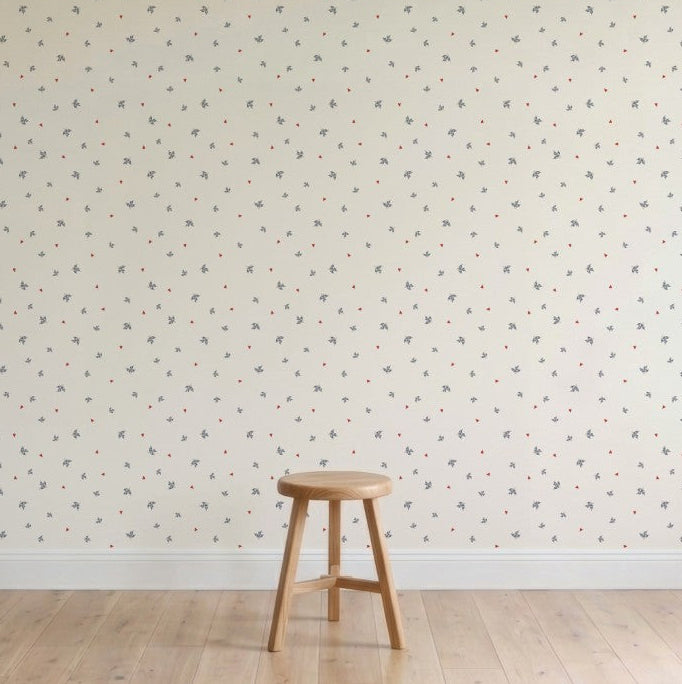 A plain wooden stool sits on a light wood floor before a cream-colored wall decorated with Soaring Hearts Wallpaper featuring subtle, muted bird designs. The minimalist scene appears calm and uncluttered.