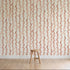 A wooden stool sits on a light wood floor in front of a cream wall featuring Wiggle Stripe Wallpaper, Red—vertical wavy red and beige stripes. The minimal, well-lit setting highlights this stylish children’s wallpaper.