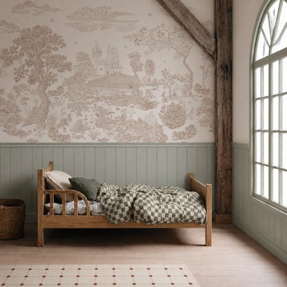 A cozy wood bed with green checked bedding sits against a wallpapered wall featuring the Forest Hideaway Mural, Neutral. A large arched window and rustic wooden beam add warmth and serenity to the bedroom, while a woven basket beside the bed completes this tranquil retreat.