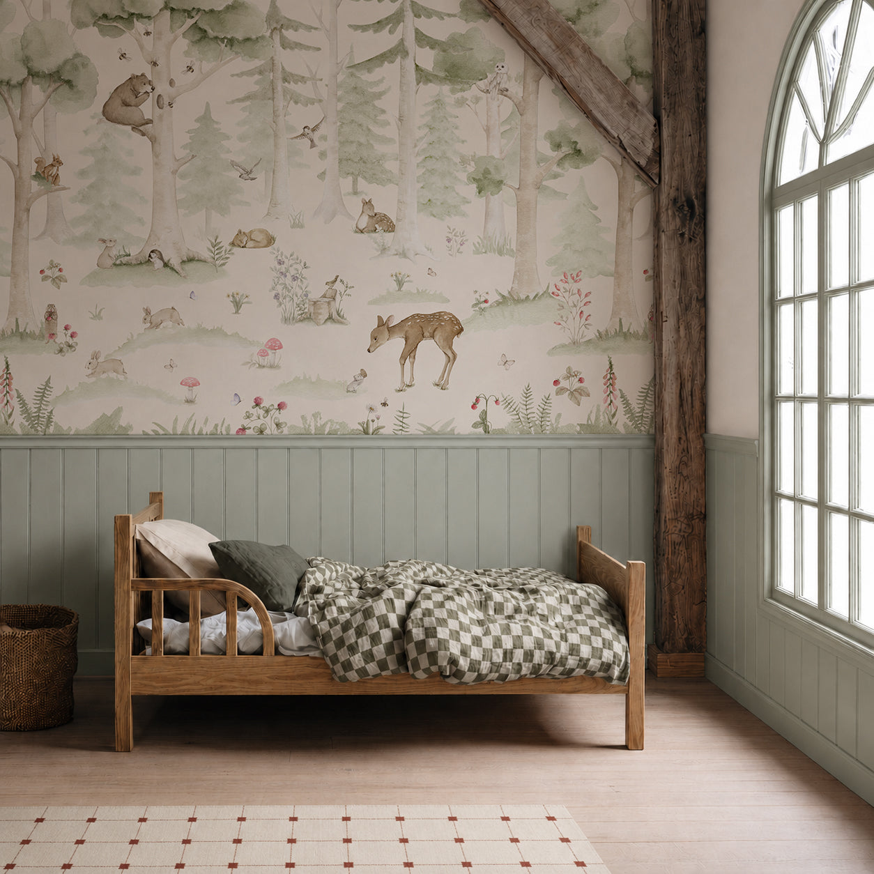 A cozy child’s bedroom features a wooden bed with green checkered bedding, a wicker basket, and the charming Woodland Friends Mural showcasing forest animals and trees on the wall. A large arched window allows natural light to fill the space.