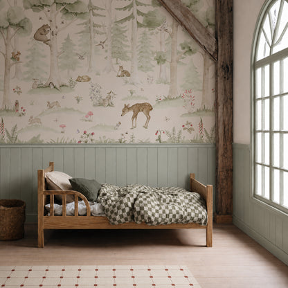 A cozy child’s bedroom features a wooden bed with green checkered bedding, a wicker basket, and the charming Woodland Friends Mural showcasing forest animals and trees on the wall. A large arched window allows natural light to fill the space.