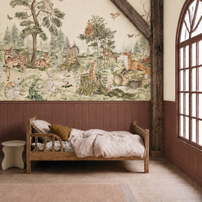 A cozy children’s bedroom features a wooden bed, striped bedding, and the enchanting “Into The Forest Mural” on the wall, depicting deer, foxes, rabbits, and trees. Sunlight pours in through a large arched window, illuminating the hand-painted mural and bringing the magical woodland scene to life.