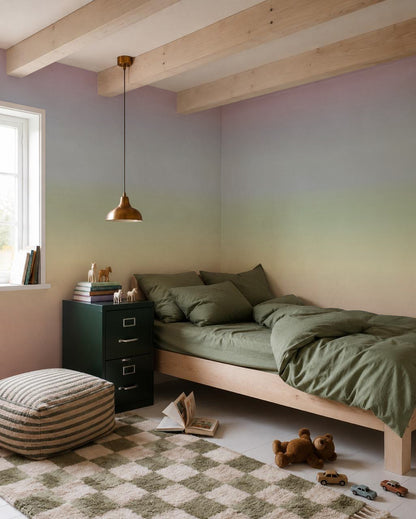 A cozy bedroom with a green bed, striped pouf, checkered rug, nightstand with books, toy animals, a window streaming sunlight, and a brass pendant light. The walls are adorned with the Ombre Mural, Rainbow—a gradient pastel wallpaper that brings a dreamy touch to the space.