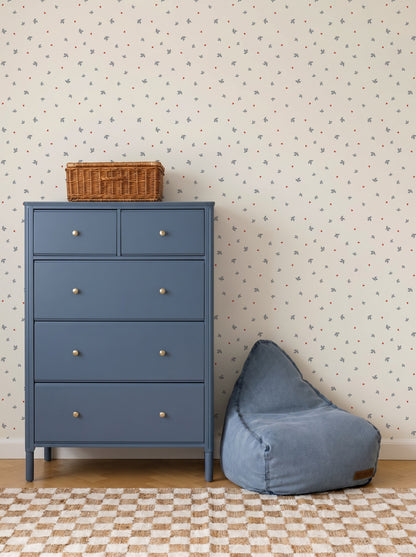 A blue dresser with a wicker basket on top stands next to a blue bean bag chair. The wall behind features Soaring Hearts Wallpaper and a small colorful print, while a checkered rug is on the floor.