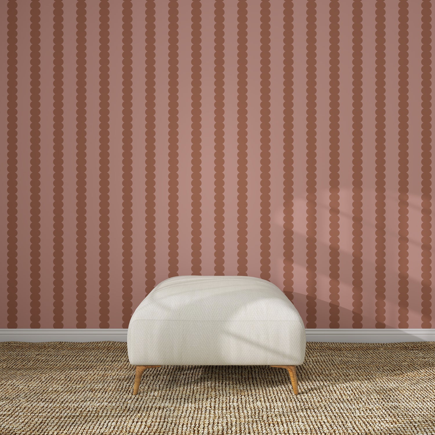 A cream-colored ottoman sits on a textured beige rug in front of Scallop Stripe Wallpaper Toffee Rose. Sunlight casts gentle shadows across the ottoman and floor, highlighting the elegant design.