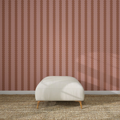 A cream-colored ottoman sits on a textured beige rug in front of Scallop Stripe Wallpaper Toffee Rose. Sunlight casts gentle shadows across the ottoman and floor, highlighting the elegant design.