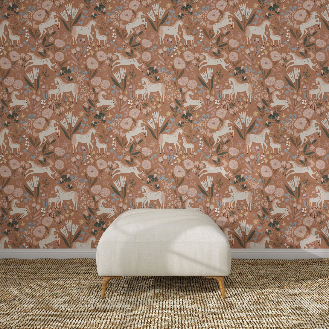 A white ottoman sits on a woven rug in front of Unicorn Meadow Wallpaper Toffee Rose, featuring pink florals, white horses, and leafy patterns for an exquisite look.