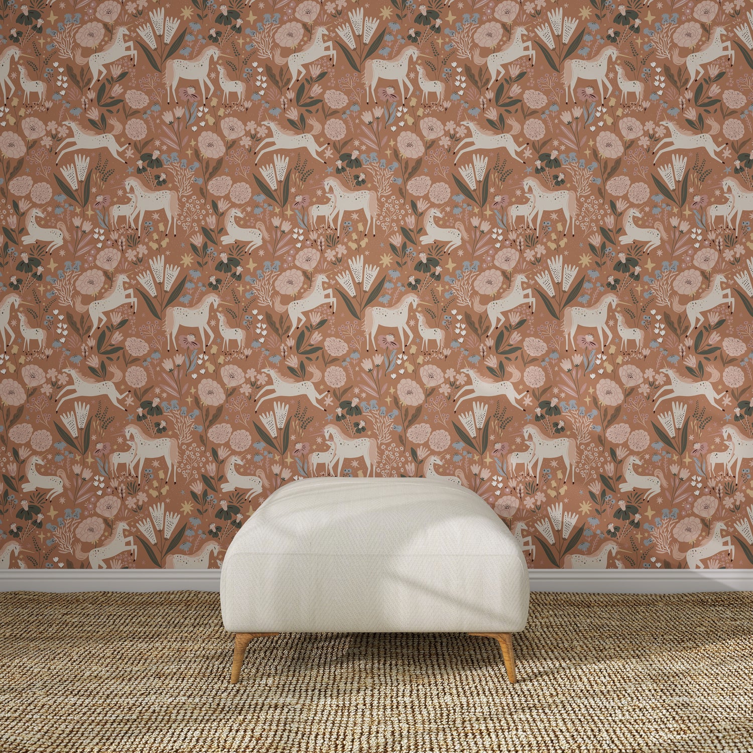 A white ottoman sits on a woven rug in front of Unicorn Meadow Wallpaper Toffee Rose, featuring pink florals, white horses, and leafy patterns for an exquisite look.