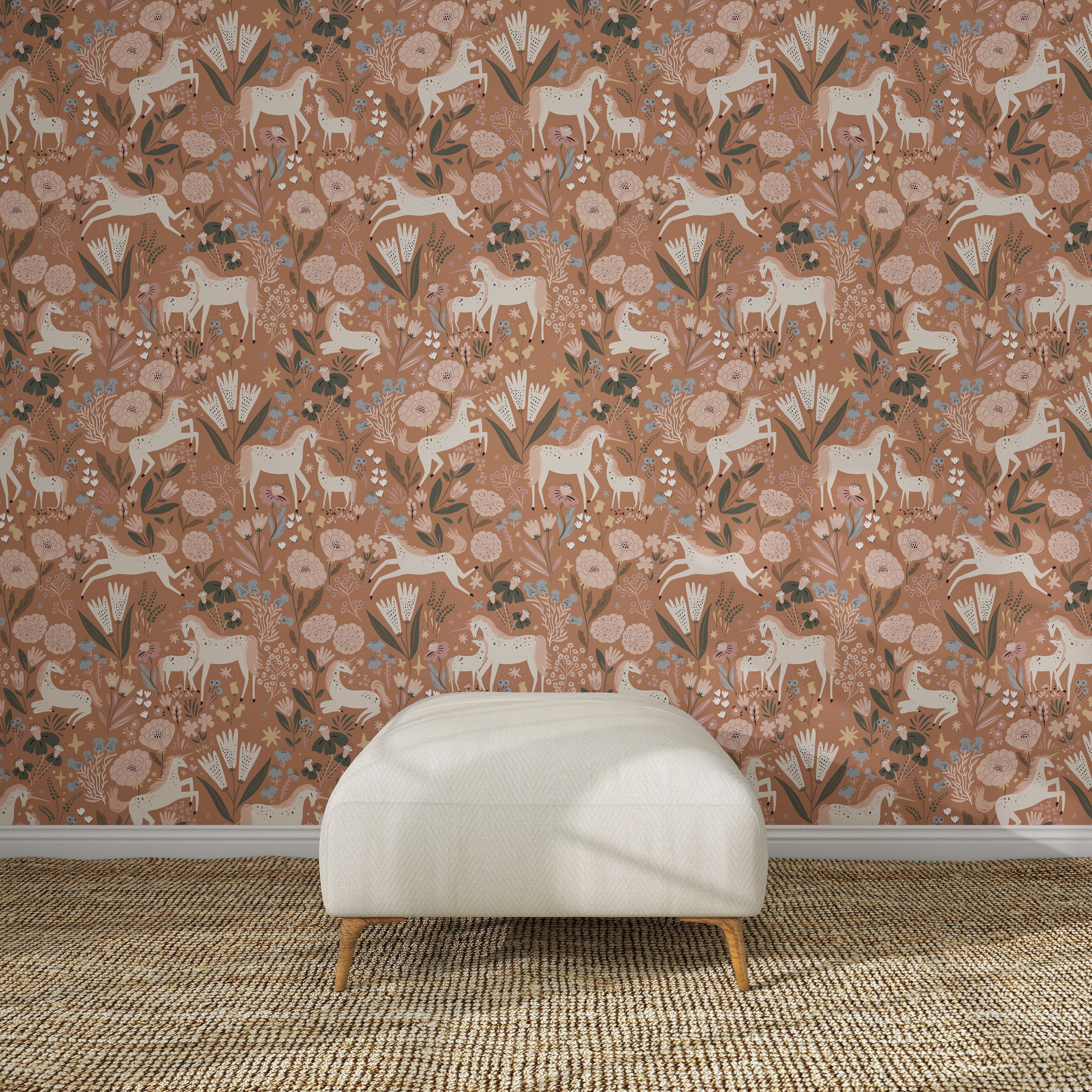 A white ottoman sits on a woven rug in front of Unicorn Meadow Wallpaper Toffee Rose, featuring pink florals, white horses, and leafy patterns for an exquisite look.