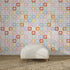 A white textured ottoman rests on a woven rug before a wall adorned with the "Floral Fun land Repeat Wallpaper Pattern | Sample," featuring vibrant, geometric floral designs in a colorful grid arrangement.