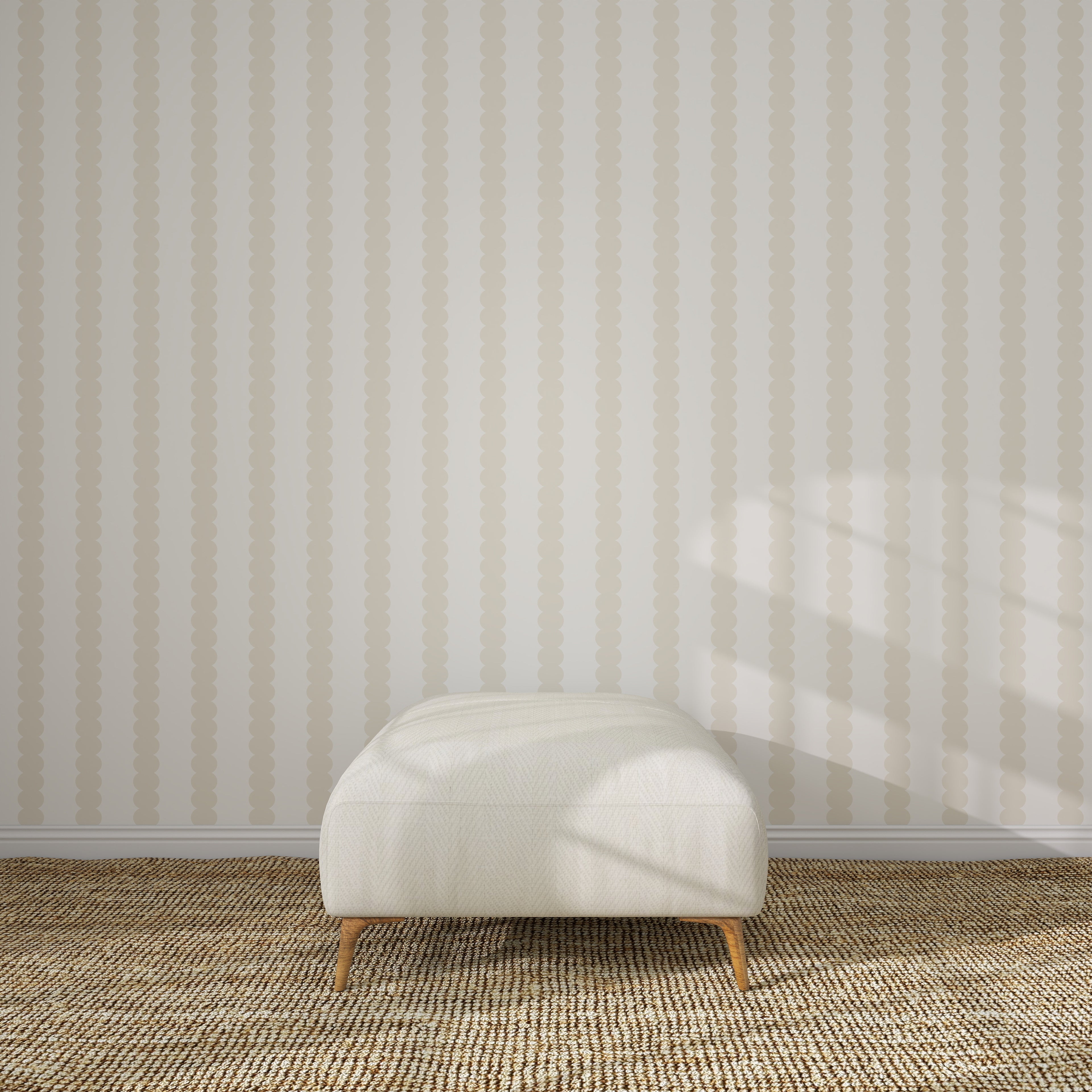 A cream-colored ottoman with wooden legs rests on a woven carpet in front of Scallop Stripe Wallpaper Cloud, as soft sunlight and window shadows play across the wall and floor.
