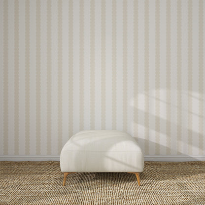 A cream-colored ottoman with wooden legs rests on a woven carpet in front of Scallop Stripe Wallpaper Cloud, as soft sunlight and window shadows play across the wall and floor.