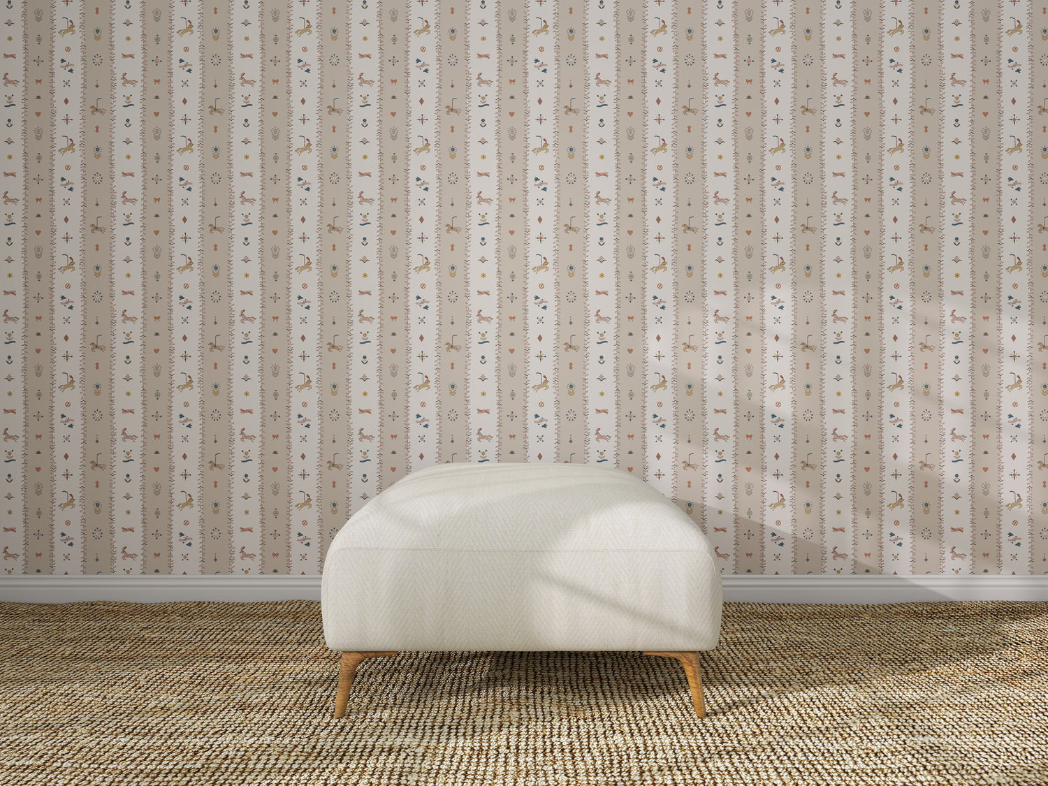 A white upholstered bench with wooden legs sits on a textured beige rug in front of The Little Carousel Stripe Wallpaper, Rose, featuring vertical stripes and delicate floral motifs.