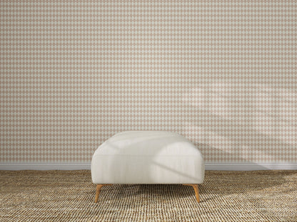 A minimalist room features a light-colored bench with wooden legs on a textured carpet, set against a wall adorned with Diamond Dancer Wallpaper in Rose, showcasing hand-drawn harlequin diamonds in beige and white.