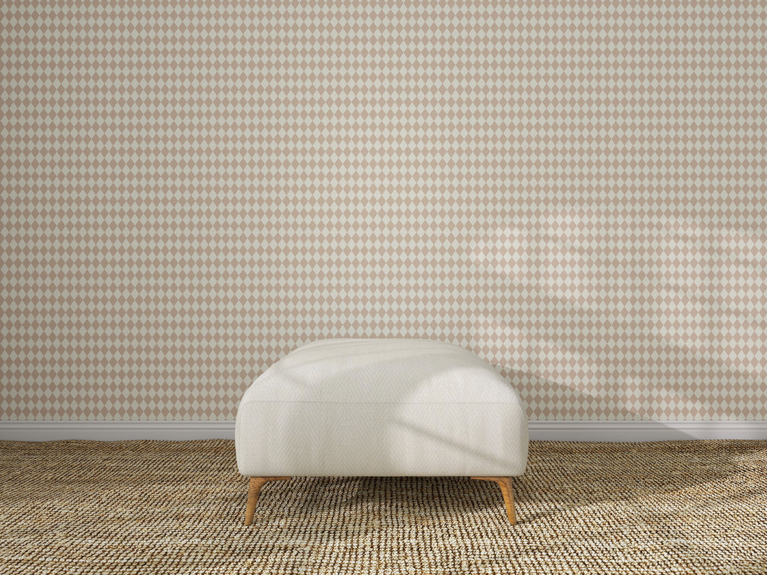 A beige ottoman sits on a woven carpet in front of a wall featuring the Diamond Dancer Wallpaper Sample in Rose. The empty, well-lit room has soft shadows on the wall and floor.