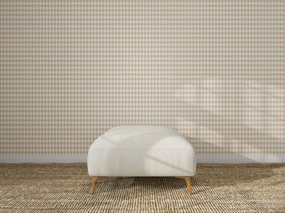 A beige ottoman sits on a woven carpet in front of a wall featuring the Diamond Dancer Wallpaper Sample in Rose. The empty, well-lit room has soft shadows on the wall and floor.
