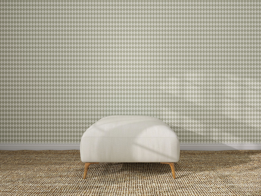 A cream-colored ottoman with wooden legs sits on a woven beige carpet, centered in front of a wall covered with Diamond Dancer Wallpaper, Green.
