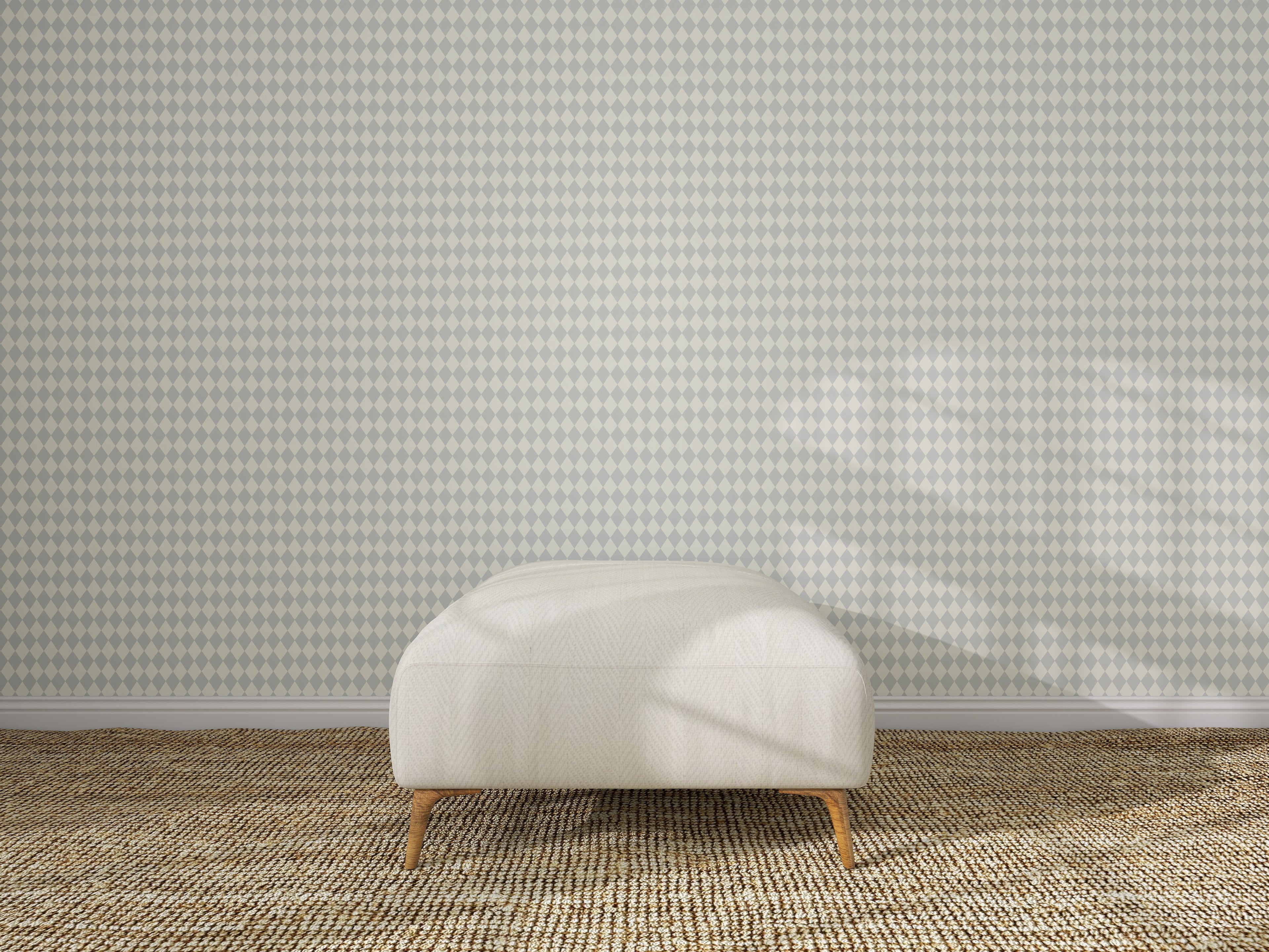 A white ottoman rests on a textured beige carpet in front of a wall adorned with Diamond Dancer Wallpaper in Blue, its subtle geometric pattern highlighted by sunlight casting gentle shadows across the floor and wall.