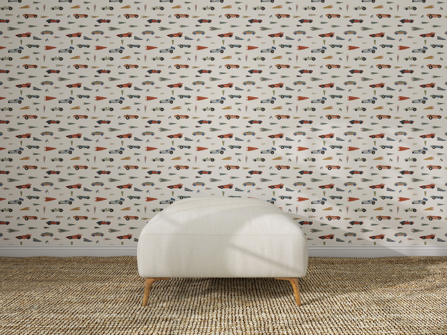 A white upholstered chair sits on a woven rug in front of nursery wall decor featuring Speedway Dash Wallpaper, which displays a playful, colorful pattern with assorted cars, trucks, traffic cones, and traffic signs.