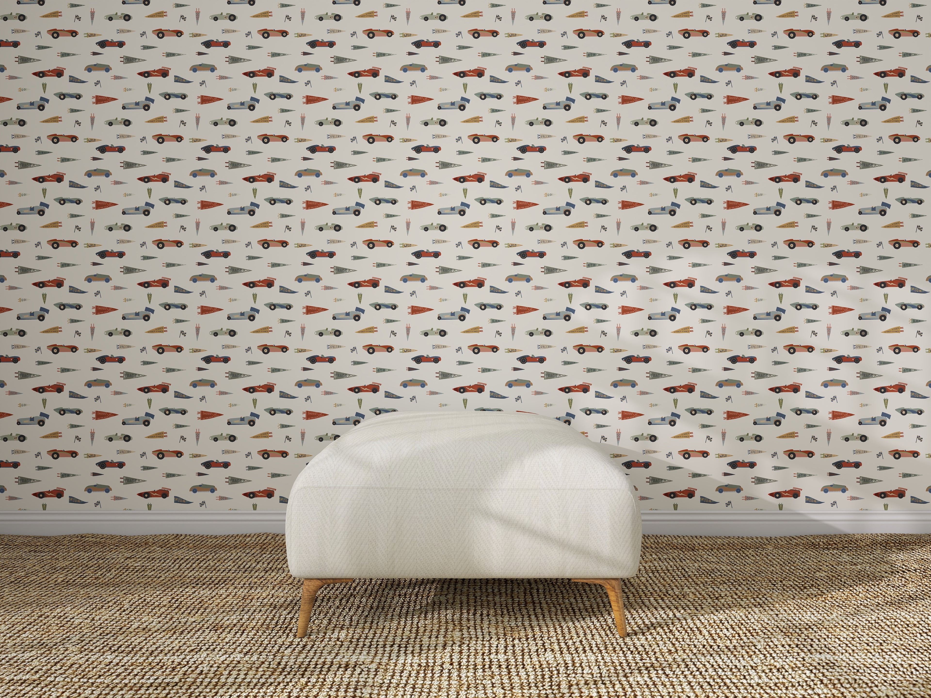 A white upholstered chair sits on a woven rug in front of nursery wall decor featuring Speedway Dash Wallpaper, which displays a playful, colorful pattern with assorted cars, trucks, traffic cones, and traffic signs.