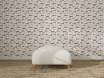 A white upholstered chair sits on a woven rug in front of nursery wall decor featuring Speedway Dash Wallpaper, which displays a playful, colorful pattern with assorted cars, trucks, traffic cones, and traffic signs.