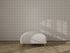 A minimalist interior showcases Checkered Wallpaper, Cream, a light upholstered bench with wooden legs, and a textured woven carpet. Sunlight casts gentle shadows, enhancing the wall decor.