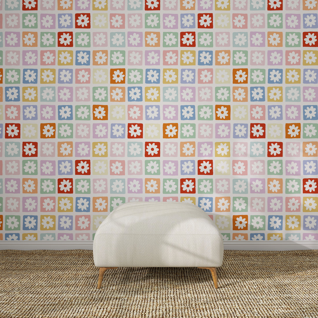 A white, cushioned ottoman sits on a textured brown rug in front of a wall decorated with the Floral Fun land Repeat Wallpaper Pattern—a vibrant retro floral design in pastel pinks, purples, blues, yellows, oranges, reds, and greens.