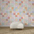 A white cushioned bench with wooden legs sits on a brown woven rug in front of a vibrant wall adorned with the Floral Funland Mural, featuring multicoloured repeating floral patterns.