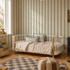 Cozy children’s bedroom featuring a round-edged bed, bookshelf, toys, woven storage baskets, a pouf, checkered rug on wooden floors, warm neutral tones throughout, and Scallop Stripe Wallpaper in Green. Large window lets in plenty of light.