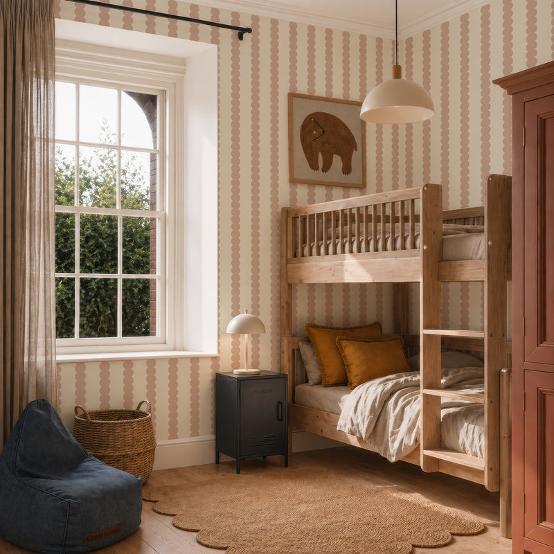 A cozy kids’ bedroom with wooden bunk beds, earth-toned bedding, a black nightstand, a round lamp, a blue beanbag, wicker basket, elephant wall art, window with curtains, and Scallop Stripe Wallpaper in Pink.