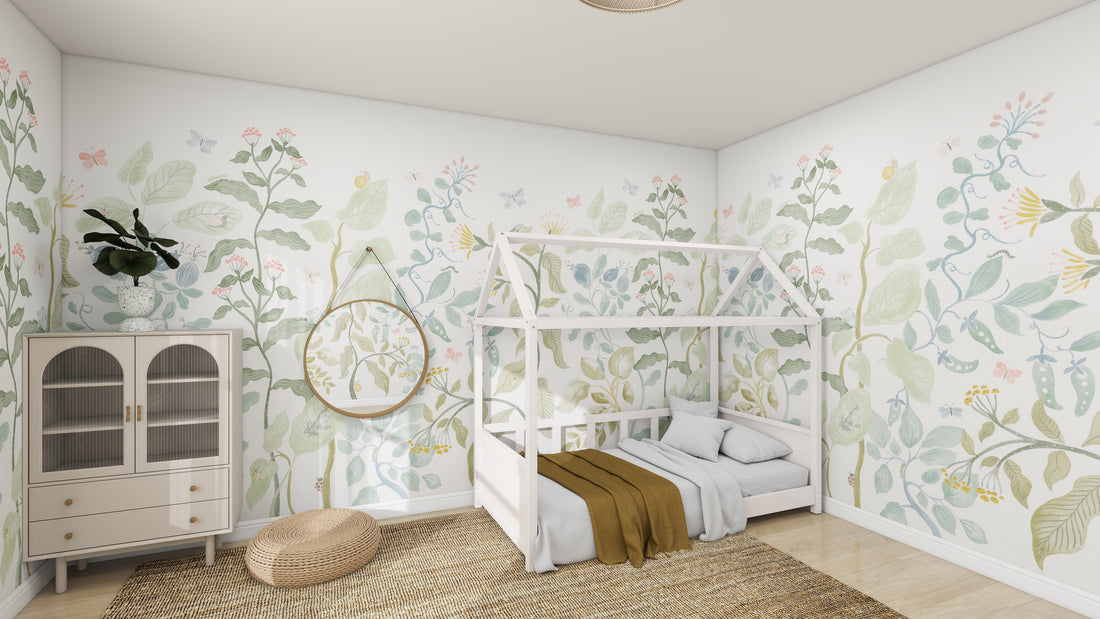 A cozy childrens room welcomes you into a whimsical world featuring a white house-shaped bed with gray and brown linens. The walls boast munks and mes Secret Garden Wallpaper Mural in green, pink, and yellow patterns. A round mirror and cabinet rest atop a woven rug on the left side of the wooden floor.