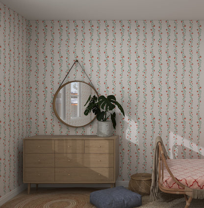 A cozy bedroom with Strawberry Stripes Wallpaper by munks and me in warm hues, a round mirror above a wooden dresser, and a potted plant. On the right is a bed with a woven headboard. A soft ottoman and circular woven rug complete the room as natural light filters through the window.