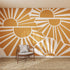 A modern room features the Sunbeams Wallpaper Repeat Pattern with stylized orange and white sunrises, a wooden chair with a gray cushion, and a woven rug. Sunlight enhances the sunshine-inspired decor.