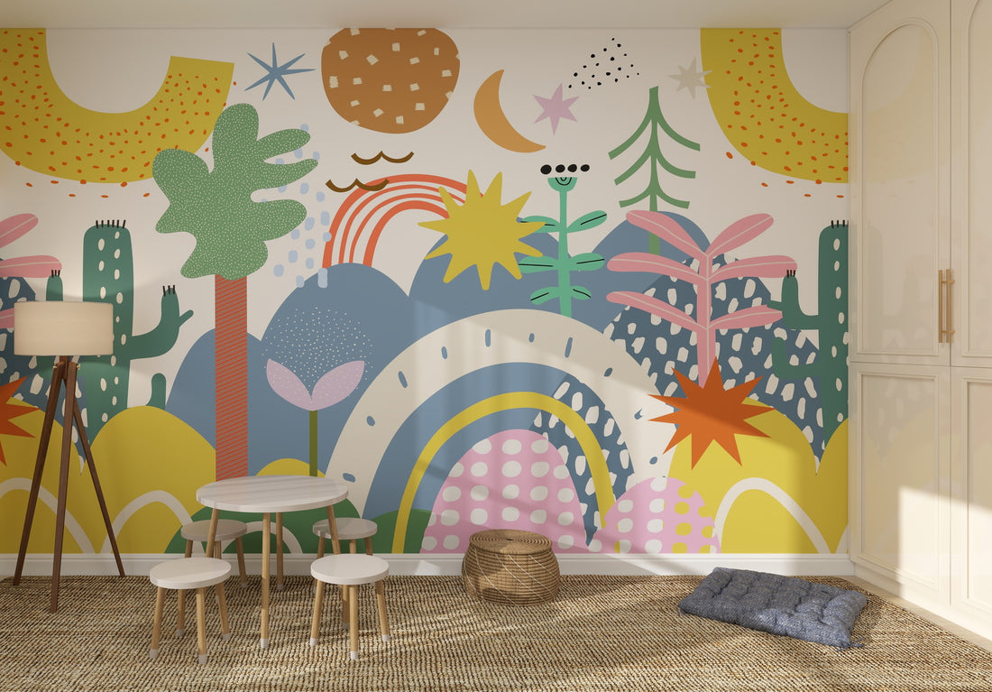 A children’s playroom featuring The Happy Wall Wallpaper Mural Sample, with colorful abstract plants, rainbows, stars, and shapes that brighten the space—paired with a round table, stools, woven rug, basket, floor lamp, and blue cushion.