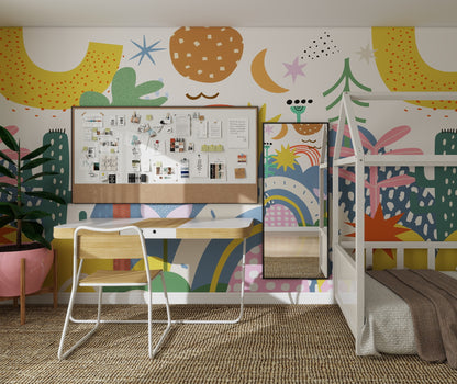 A colorful kids’ room features The Happy Wall Wallpaper Mural with playful abstract patterns, a desk and chair, a corkboard with notes and photos, a mirror, a plant in a pink pot, and a bed with a white frame.