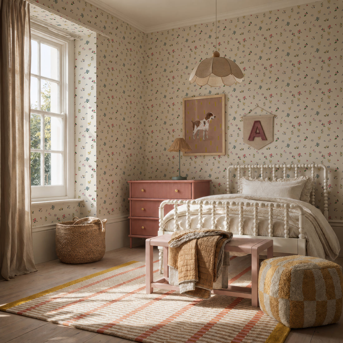 A cozy, sunlit bedroom features vibrant Powdered Petals Wallpaper, a white metal bed, pink dresser, woven basket, pouf, soft striped rug, framed dog art, and a letter A wall hanging for a warm and inviting feel.