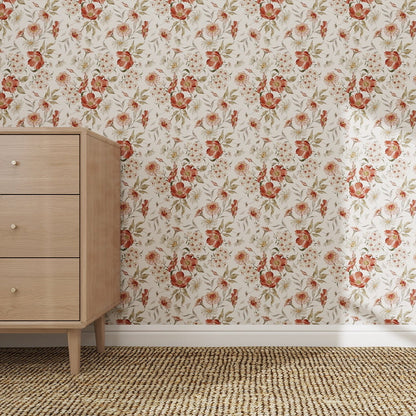 A light wooden three-drawer dresser stands on a woven rug by a wall adorned with Wild Rose Dreams Wallpaper Repeat Pattern, featuring vivid red and orange flowers with green leaves. The scene feels simple, cozy, and vintage.