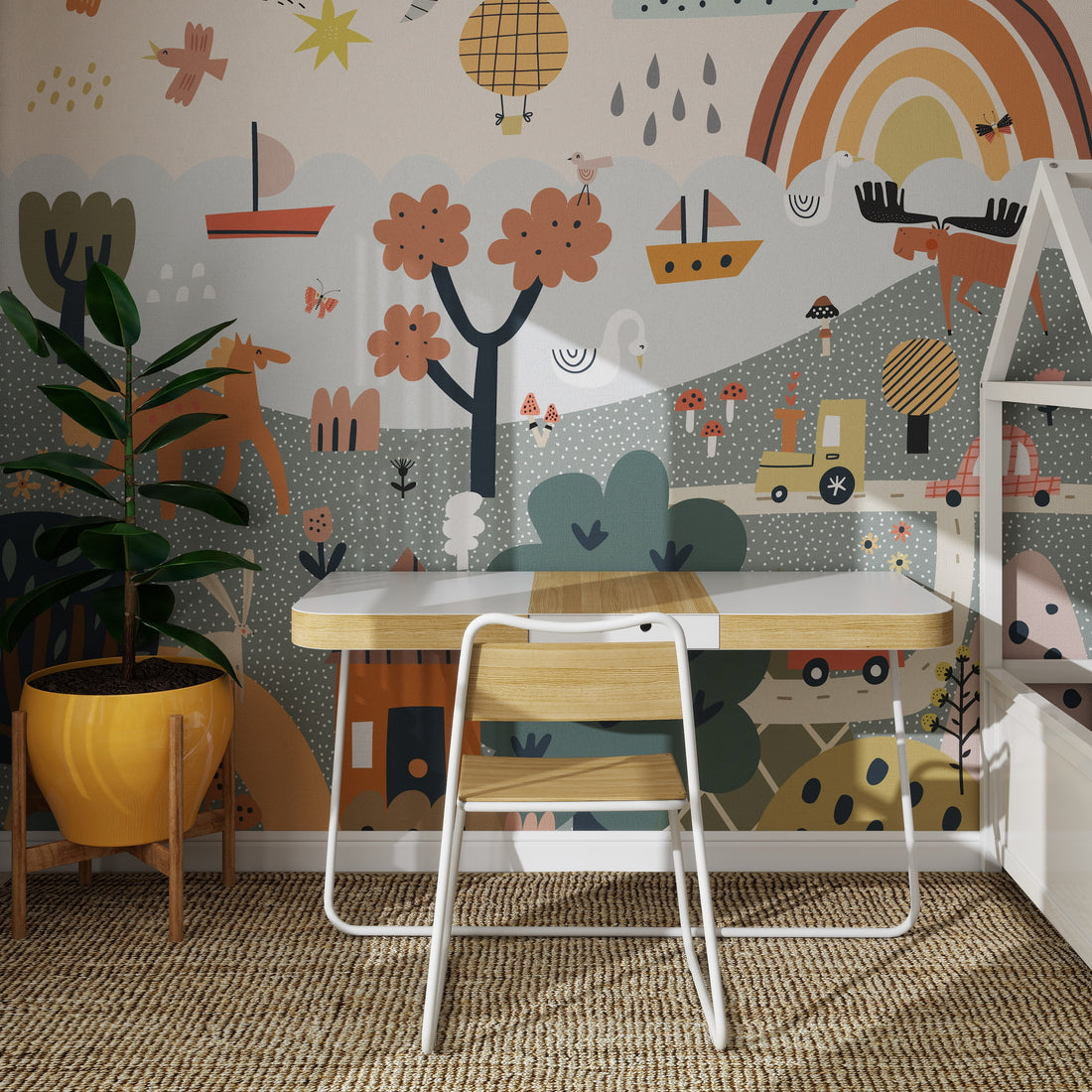 A small wooden desk with a white chair stands on a woven rug before the Wonderpark Wallpaper Mural—a colorful, whimsical rainbow scene with trees, boats, and playful shapes. A potted plant is placed to the left of the desk.