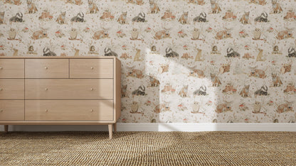 A light wood dresser rests on a woven rug by a wall adorned with the Woodland Wonder Repeat Pattern wallpaper in soft, muted tones featuring rabbits and florals. Sunlight casts gentle shadows across this charming scene.