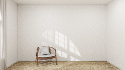 A wooden chair with a cushion sits on a woven rug in a bright, empty room featuring Hallie Leopard Print Wallpaper Repeat Pattern in light pink. Sunlight streams through the window, casting shadows on the wall.