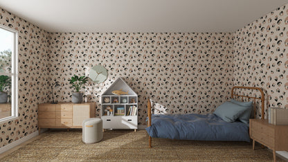 A cozy bedroom features Yara Leopard Print Wallpaper Repeat Pattern, a wooden bed with blue bedding, a house-shaped bookshelf, a plant-topped dresser, a round ottoman, and a large window that fills the space with natural light.