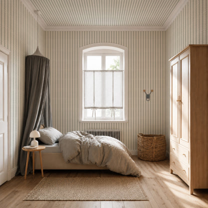 Cozy bedroom with a canopy bed, light bedding, small round side table and lamp, wicker basket, wooden wardrobe, and Little Abacus Stripe Wallpaper in Blue and Green. Sunlight streams through a window with sheer curtains.