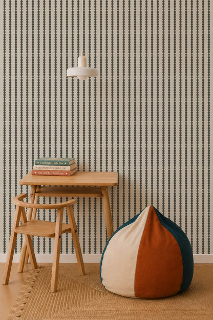 A minimalist room features a small wooden desk and chair, a stack of books, a round color-blocked bean bag, a woven rug, a pendant lamp, nursery decor for a calming vibe, and Little Abacus Stripe Wallpaper in Forest with vertical stripes on the wall.