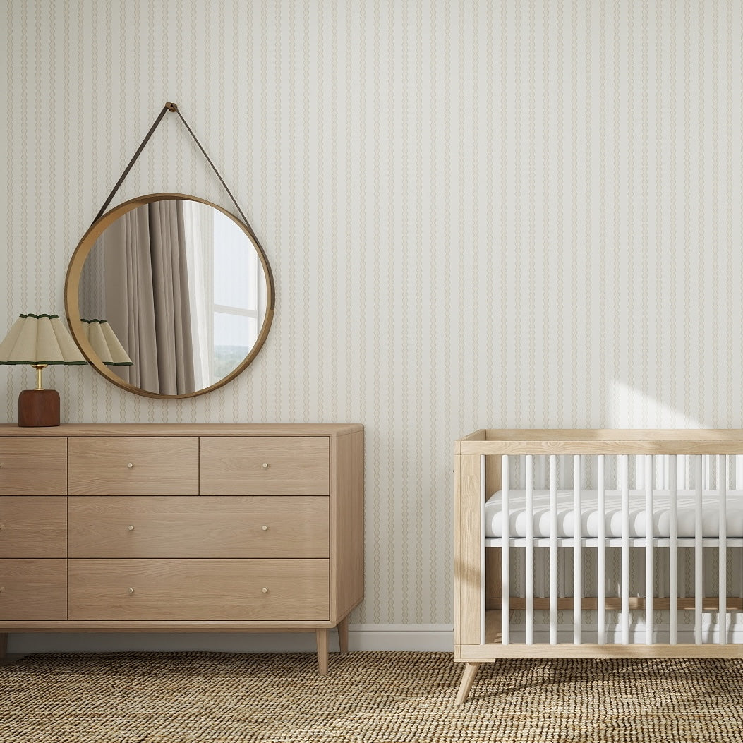 A minimalist nursery pairs a light wood crib, matching dresser, round mirror, lamp, and textured rug with Little Abacus Stripe Off White and Taupe Wallpaper Sample for a calm, neutral look. Ideal for wallpaper inspiration from online imagery.