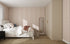 A cozy bedroom features a bed with white bedding, a black nightstand and lamp, floor mirror, beige wardrobe, and sunlight streaming onto the Little Abacus Stripe Rose Wallpaper Sample, highlighting its quality and color.