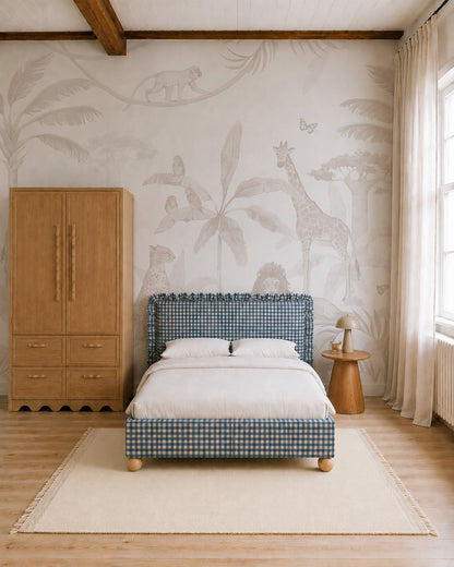 Minimalist bedroom featuring a blue plaid bed, light bedding, wooden wardrobe and side table, large window, and the African Safari Mural, Neutral—a nursery mural showcasing animals and plants in soft neutral tones. Natural light fills the space.