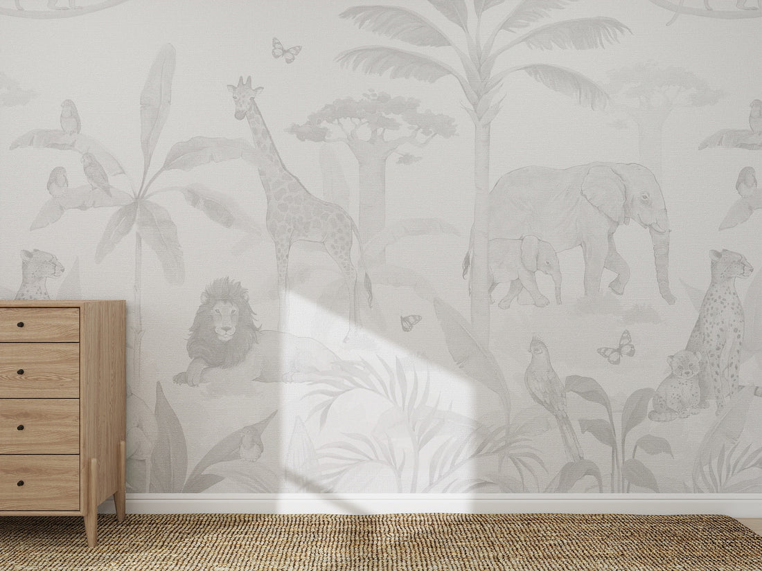 A children’s room with a light wood dresser, woven rug, and the African Safari Wallpaper Mural in grey, featuring giraffes, elephants, lions, parrots, and cheetahs among trees and plants in soft neutral shades.