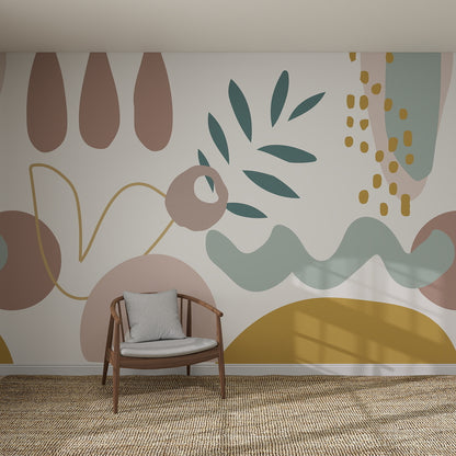 A wooden chair with a gray cushion sits before the Abstract Wallpaper Mural, which showcases muted pink, green, yellow, and blue shapes. Sunlight gently casts soft shadows across the rug and wall.