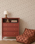 A rust-colored dresser with books, a teddy bear, and a polka-dot lamp sits beside a brown checked lounge chair against Berry and Bramble Wallpaper in a cozy room.